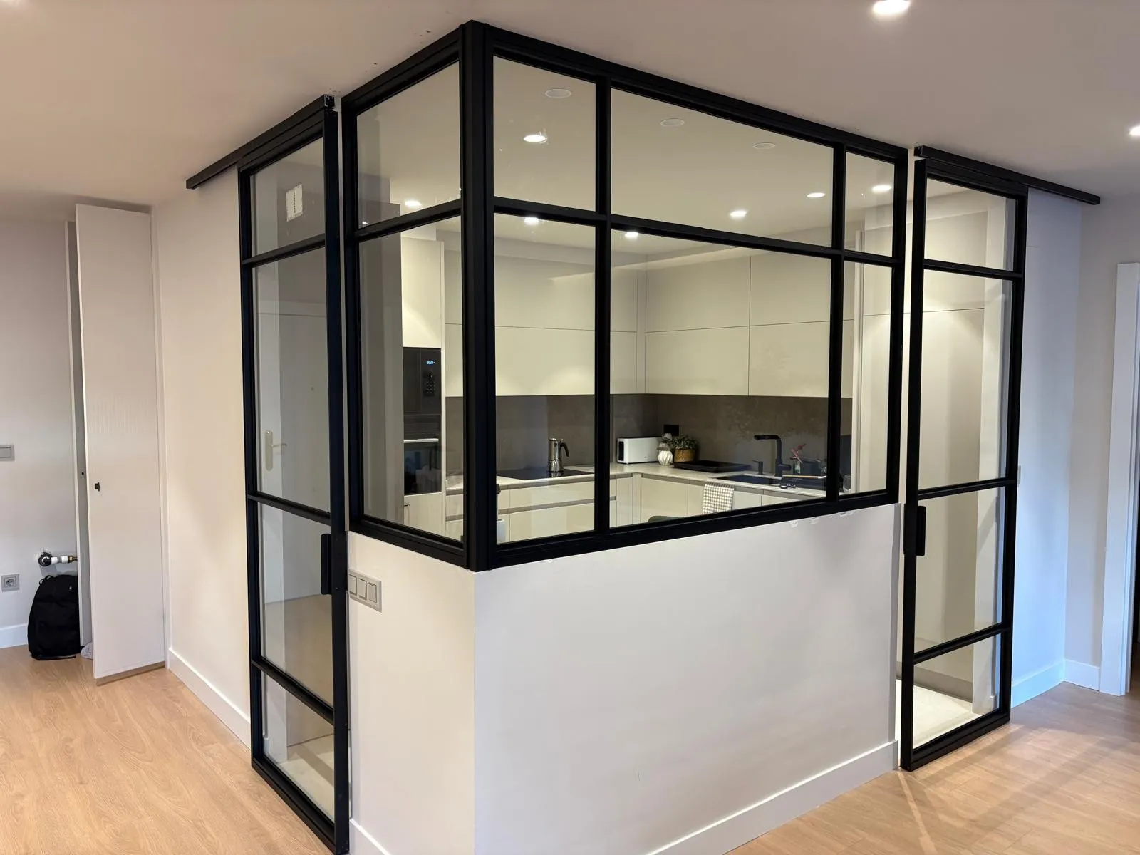 Cerramiento de vidrio con perfilería negra que separa la cocina del salón, con dos puertas correderas